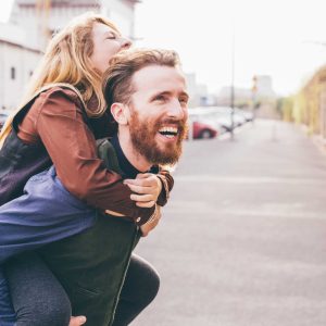 Couple of young beautiful redhead and blonde millennial woman and man, she is riding piggy back, both laughing - love, relationship, laughing concept